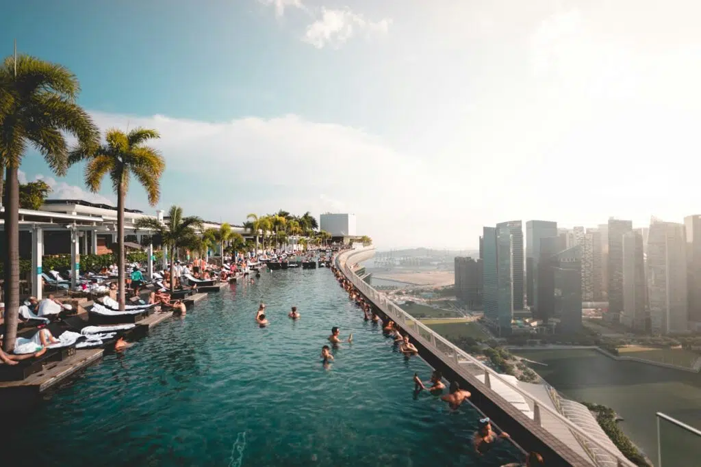 Des clients dans la piscine perchée au sommet d'un hôtel de luxe de Singapour admirent la skyline de la ville état.
